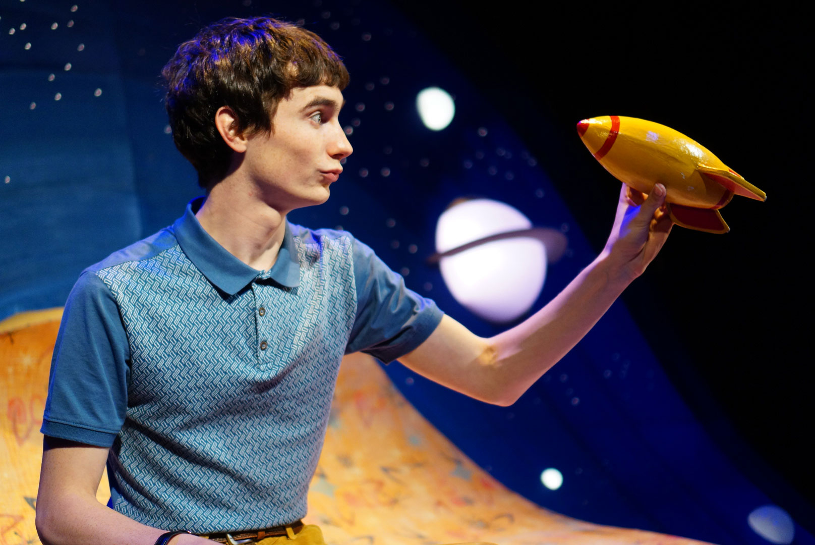 Alfie playing with a yellow rocket. He is wearing a blue top and there is a planet behind him.