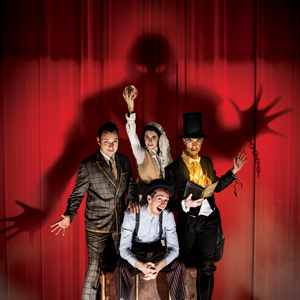 Four performers in front of a red curtain with the shadow of a ghost behind them