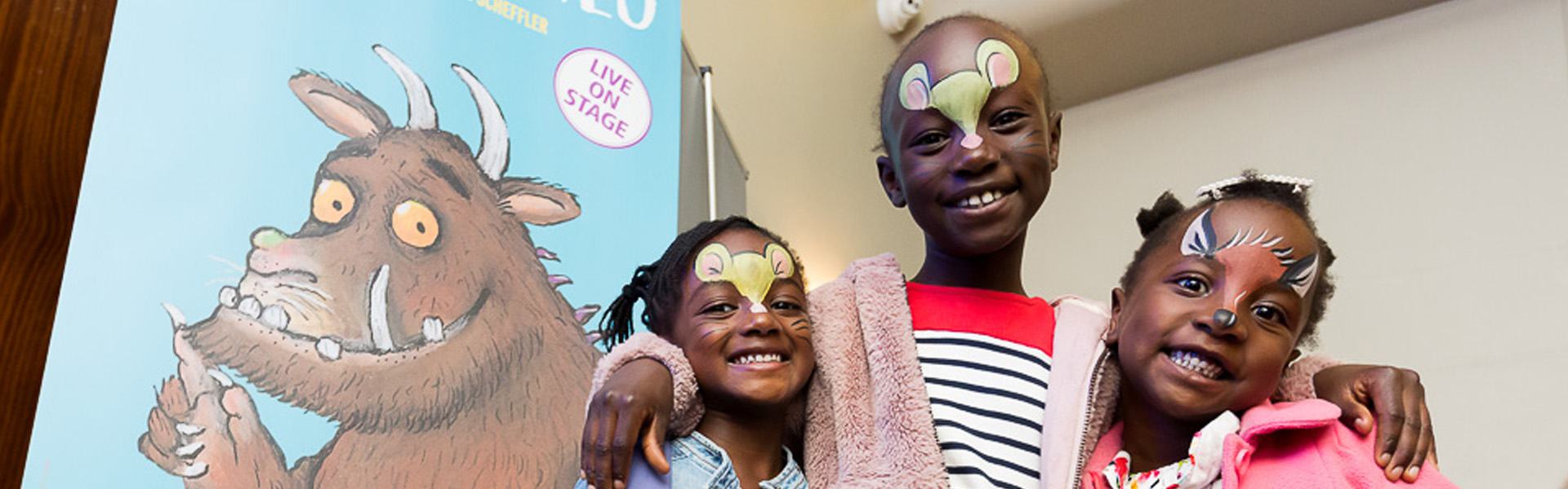 Three girls with their faces painted in front of a poster for The Gruffalo