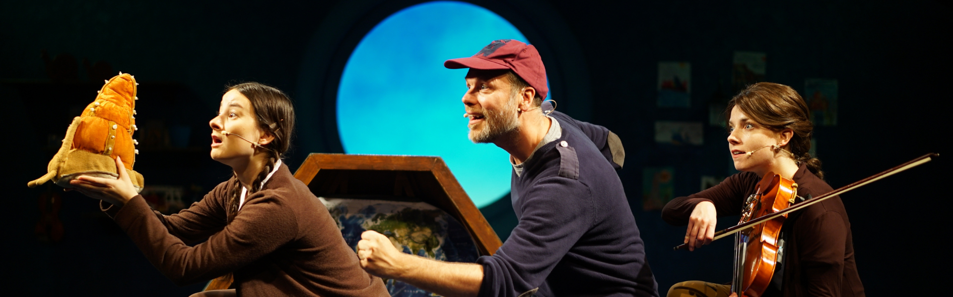 girl holding a snail with father ina. blue jumper behind and woman with a viola in the back of the line
