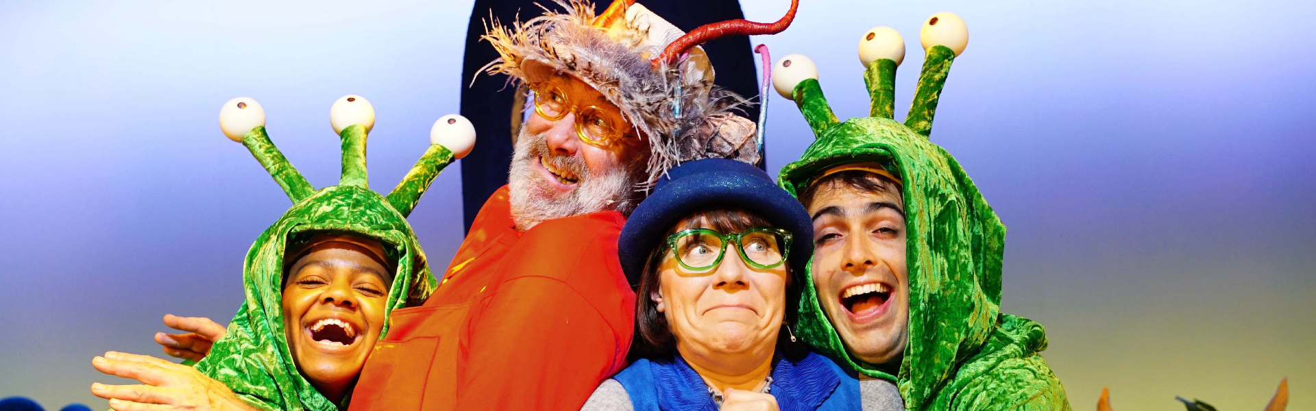Two green aliens with three eyes on their heads hugging Granfather Smed and grandmother Smoo. Grandfather has an orange top on and red antennae. Grandmother is wearing a blue waistcoat and blue hat