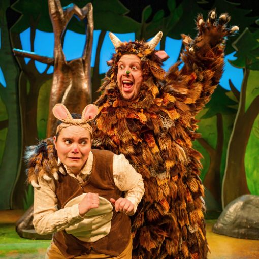 Actor in mouse costume cowering below an actor in Gruffalo costume who joyfully looks like they are about to eat the mouse.