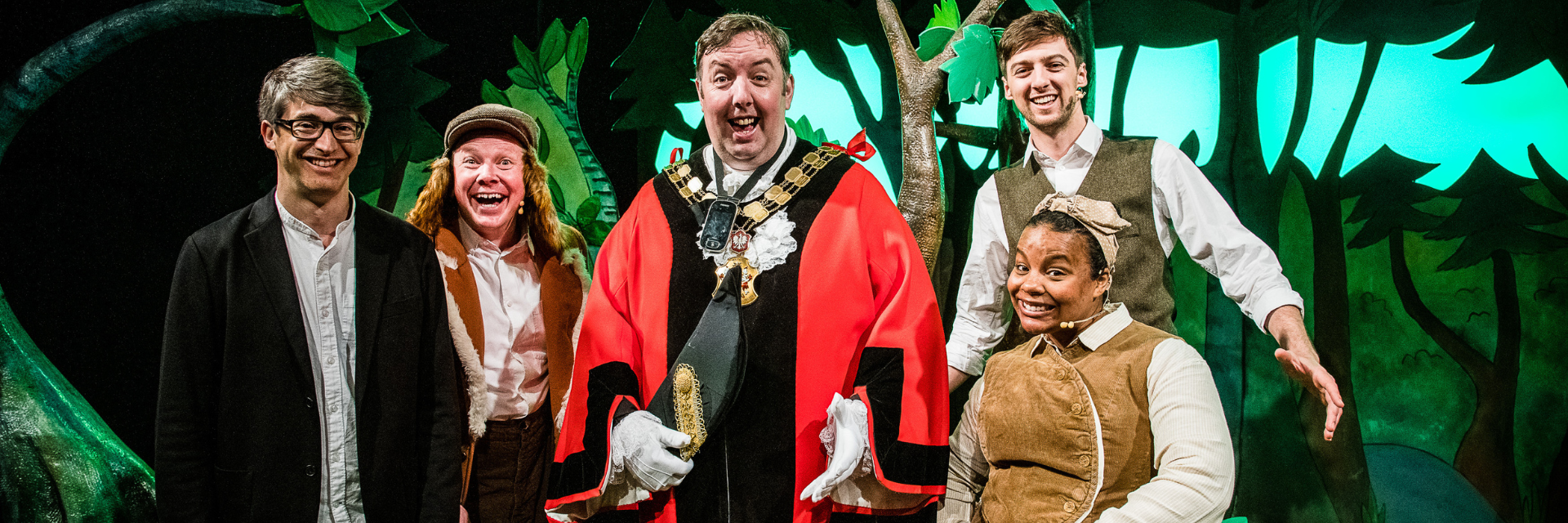 A shot of the Mayor with the cast of The Gruffalo and Toby Mitchell, artistic director of Tall Stories. They are stood in front of the set of the Gruffalo. Toby is wearing a suit jacket and white shirt, the Gruffalo cast are in their costumes and the mayor is in a red robe.