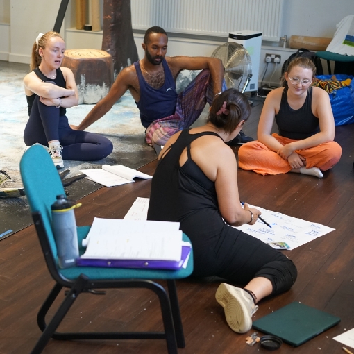 Actors and director sitting on the floor in discussion during rehearsals