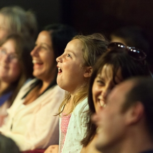 A photo taken of the audience with adults and children cheering and clapping